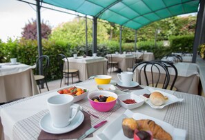 An outdoor dining area with tables and chairs, covered by a green canopy, and surrounded by greenery. - Al Fiore (Peschiera del Garda)