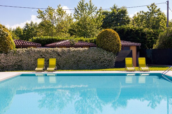 A swimming pool with two yellow lounge chairs, surrounded by a hedge and trees. - Al Fiore (Peschiera del Garda)