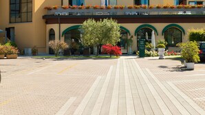 A hotel with a yellow facade, large windows, and a covered outdoor seating area with potted plants. - Al Fiore (Peschiera del Garda)