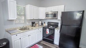 Una cocina con armarios blancos, un microondas de acero inoxidable, un refrigerador negro y una encimera con fregadero y estufa.