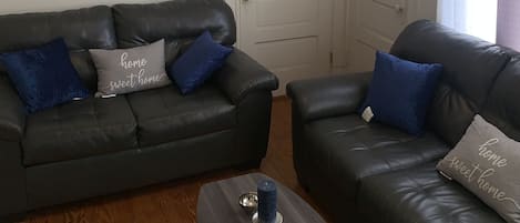 Una sala de estar con un sofá de cuero negro, una mesa de centro y un reloj de pared.