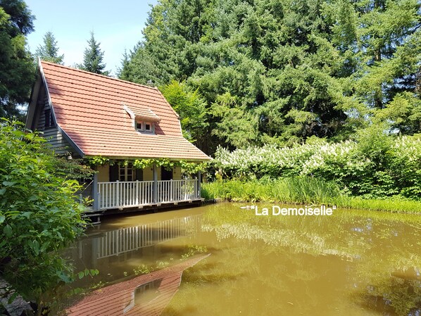 Ein Haus mit rotem Dach, weißem Veranda und Teich davor.