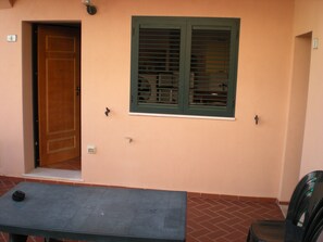 A room with a wooden door, a window with shutters, a table, and a chair.
