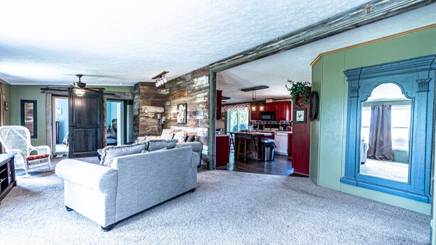 A spacious living room with a grey sofa, a white armchair, and a kitchen area visible through an open doorway. - Quiet and secluded country escape (Ashley)