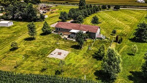 A large, single-story house with a red roof, surrounded by a well-maintained lawn and several trees. - Quiet and secluded country escape (Ashley)