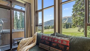 A cozy room with a large window offering a view of a mountainous landscape. - Rare Ski In Ski Out Top Floor Corner Unit! (Sun Peaks)