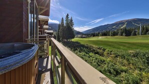A balcony with a hot tub, overlooking a golf course and mountains. - Rare Ski In Ski Out Top Floor Corner Unit! (Sun Peaks)