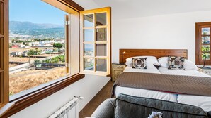 Un dormitorio con un ventanal grande, una cama con muchas almohadas y una mesita de noche.