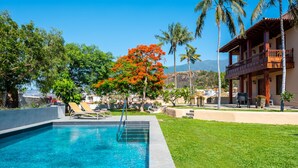 Una piscina con agua cristalina azul, rodeada de césped cuidado y palmeras.