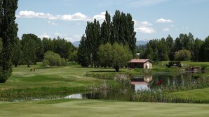 Um campo de golfe com lago, árvores e um pequeno edifício.