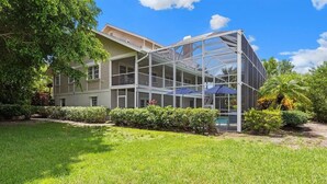 A two-story house with a glass-enclosed porch, a swimming pool, and a well-maintained lawn. - Gorgeous Fairway Facing Estate with Pool in the Dunes Golf and Country Club (Sanibel)