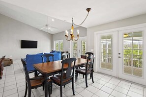 A dining area with a wooden table and chairs, a chandelier, and a television on the wall.