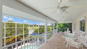 A covered outdoor area with a pool, white furniture, and a view of a golf course. - Gorgeous Fairway Facing Estate with Pool in the Dunes Golf and Country Club (Sanibel)