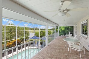 A covered outdoor area with a pool, white furniture, and a view of a golf course.