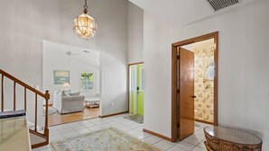 A spacious hallway with a wooden staircase, a hanging light fixture, and a wicker basket on a stand. - Gorgeous Fairway Facing Estate with Pool in the Dunes Golf and Country Club (Sanibel)
