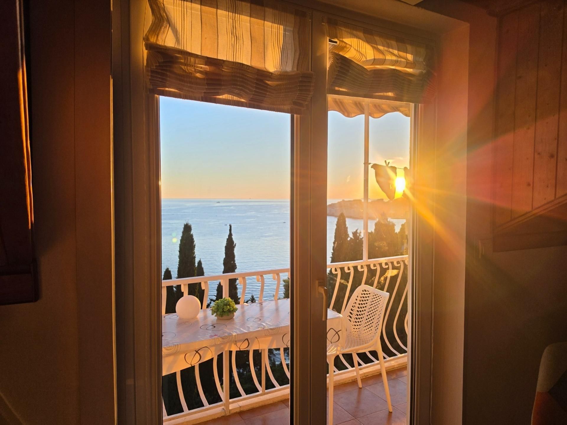 Ein Balkon mit Blick aufs Meer, ein weißer Stuhl und ein kleiner Tisch mit einer Pflanze.