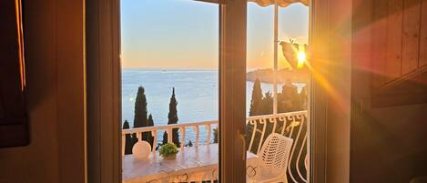Ein Balkon mit Blick aufs Meer, ein weißer Stuhl und ein kleiner Tisch mit einer Pflanze.