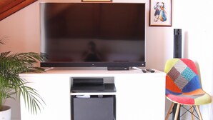 Ein Flachbildfernseher auf einer weißen Unterhaltungseinrichtung, ein farbenfroher Sessel und ein Blumentopf.