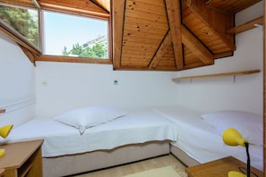 Een kleine kamer met een enkel bed, schuine plafond, een raam en een bureau met lamp.