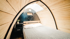 A cozy, curved wooden room with a bed, a small table with a cactus, and a window with a view of the sky. - Refugio Suncamal By Rotamundos (Cumanda)