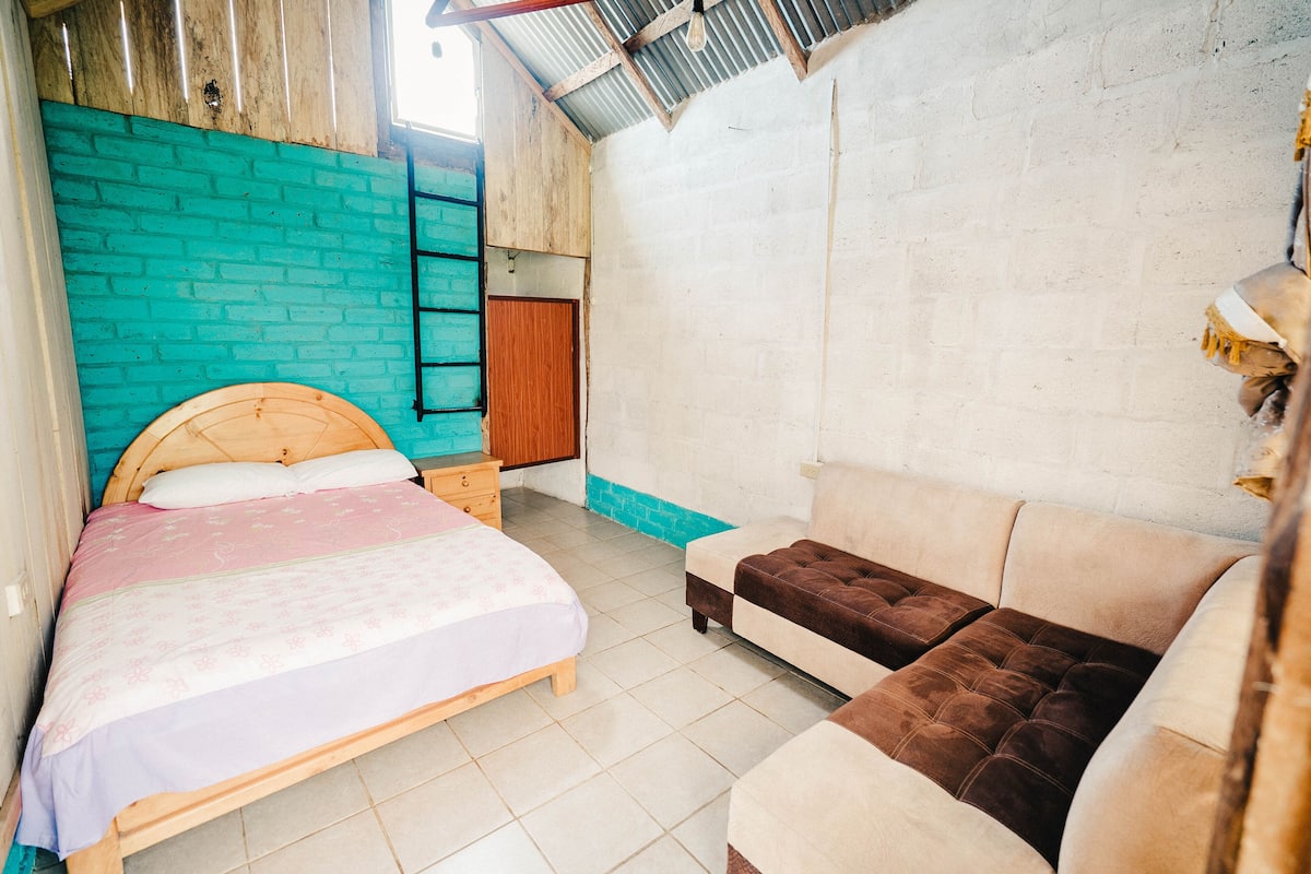 A bedroom with a bed, a sofa, a wooden wardrobe, and a blue brick wall.