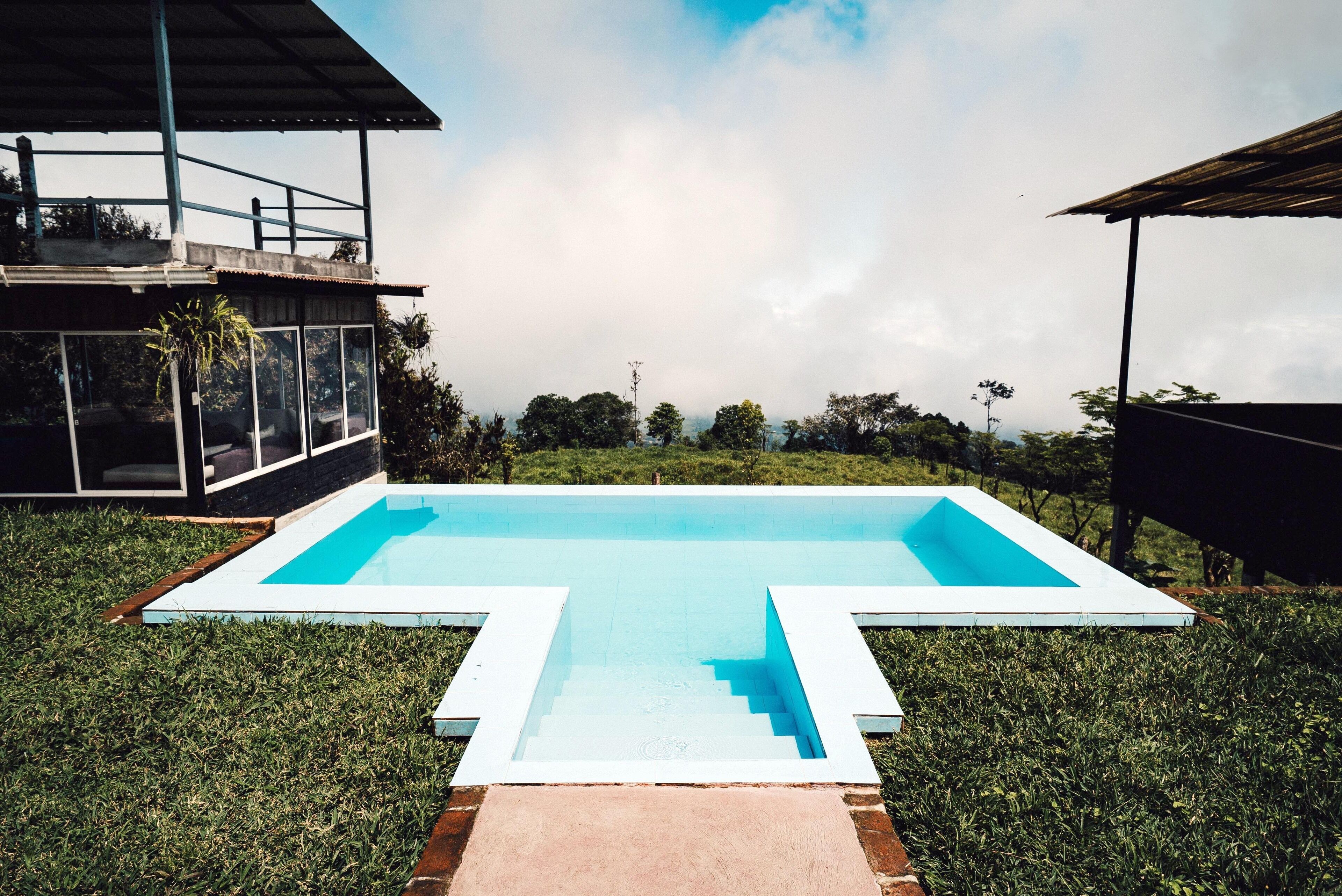 A swimming pool with a geometric design, surrounded by well-maintained grass, and adjacent to a modern building with large windows and a balcony.