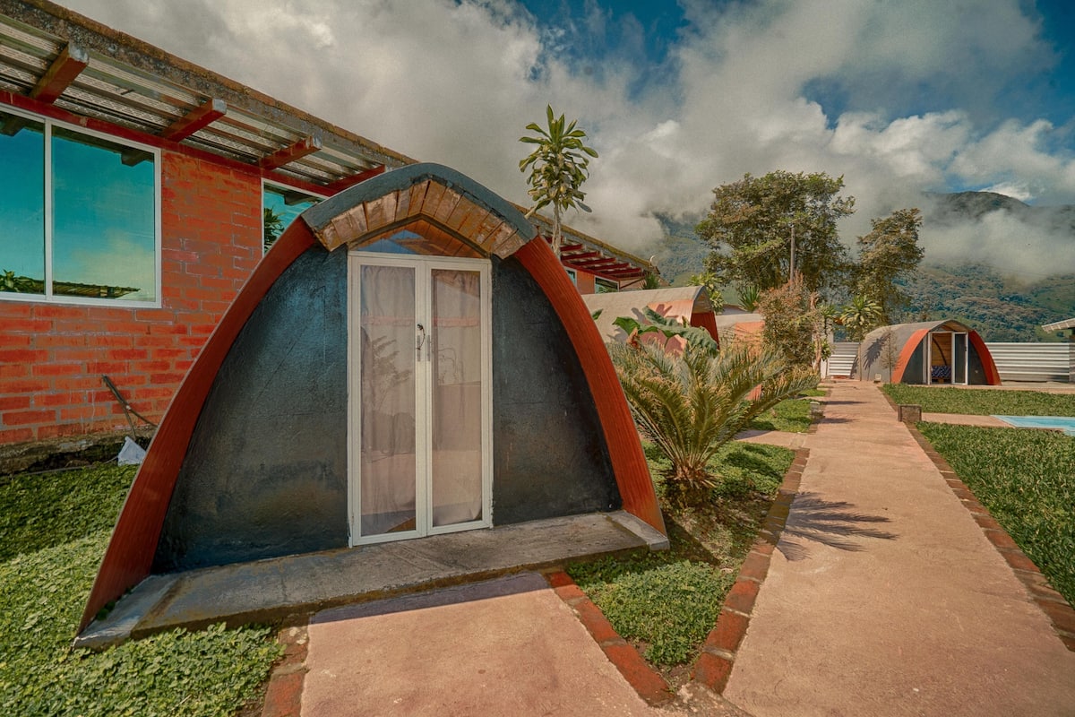 A modern building with a unique arched entrance, a brick facade, and a pathway leading to a pool area.