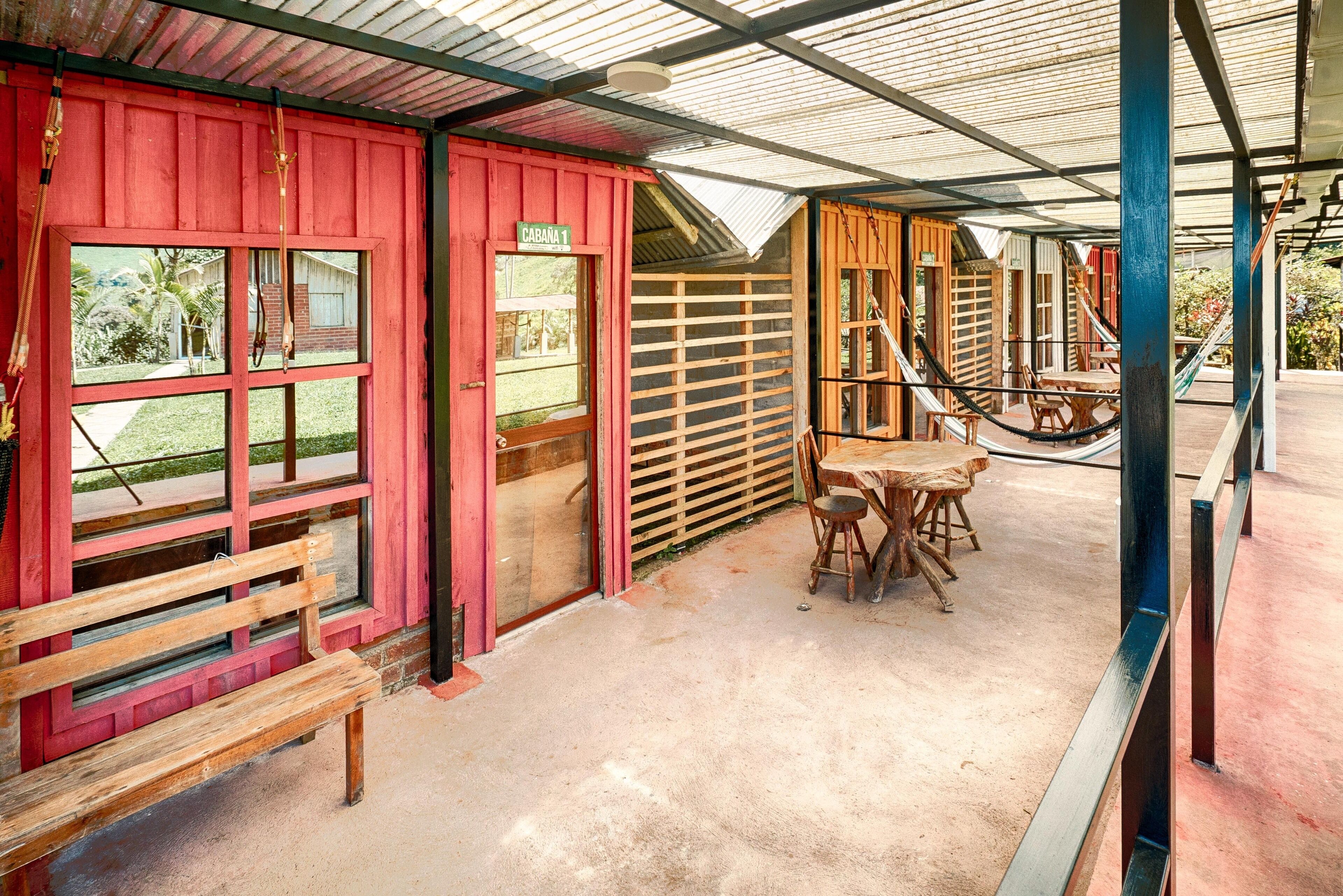 A rustic wooden building with a red exterior, a bench, and a table with chairs.