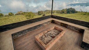 A covered outdoor area with a fire pit, brick walls, and a view of a green landscape and mountains. - Refugio Suncamal By Rotamundos (Cumanda)