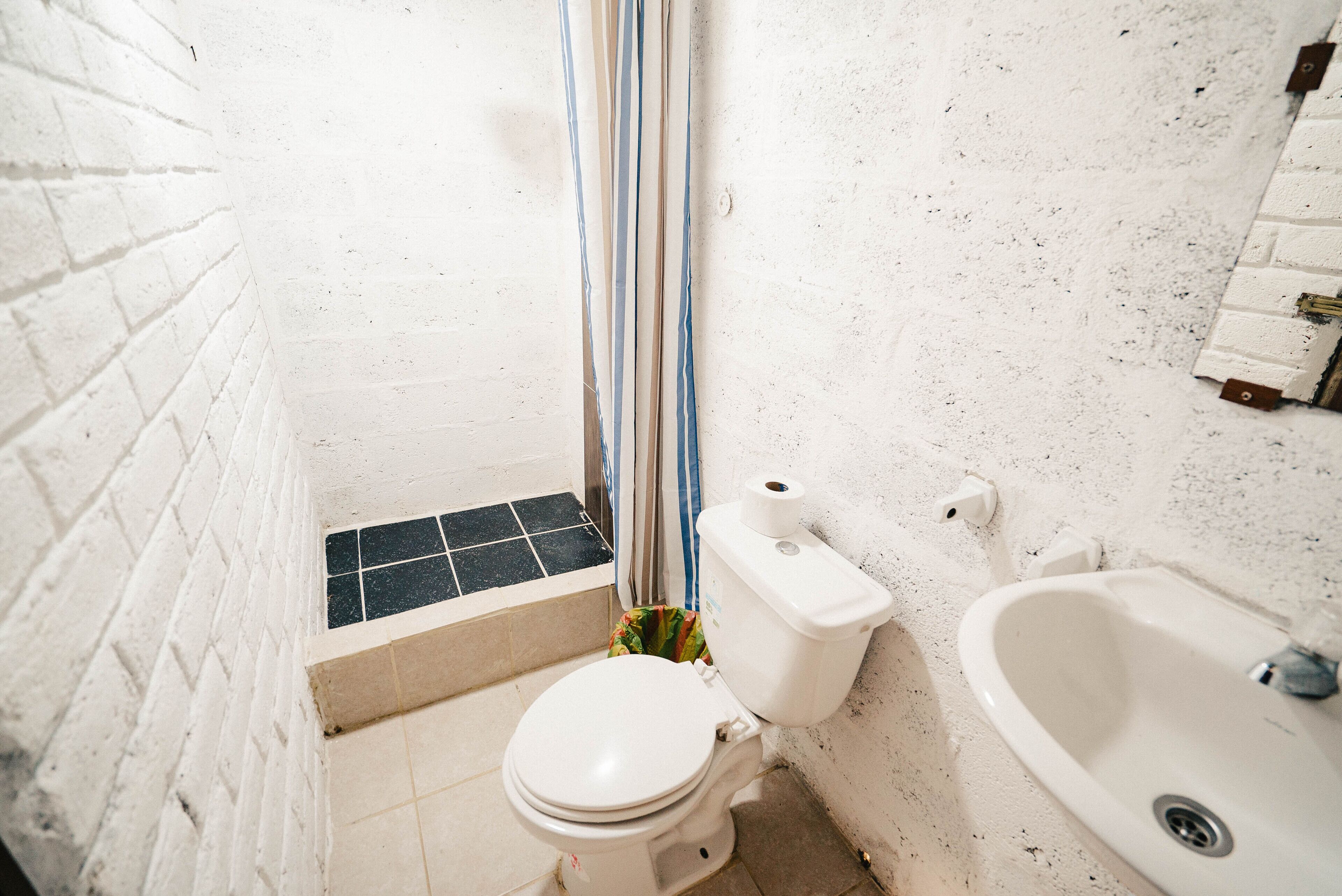 A small, narrow bathroom with a white toilet, a sink, and a shower area.