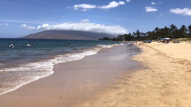 Ein Strand mit blauem Himmel, ruhiger See und einem Berg im Hintergrund.