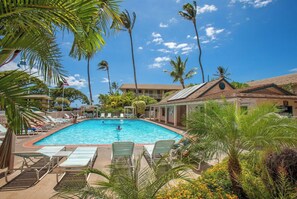 A swimming pool with lounge chairs, palm trees, and a building with a tiled roof.