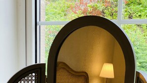Un dormitorio con cama, almohadas, una lámpara y una ventana con vistas a zonas verdes.