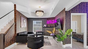 Een moderne woonkamer met een trap, een kroonluchter, een flatscreen-tv en een neonbord.