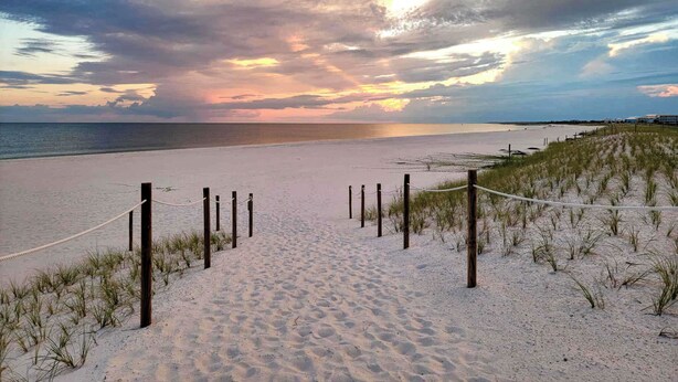 Ein Strandweg, der zum Meer führt, mit einem Zaun und einer Seilsperre.