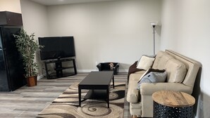 Ein modernes Wohnzimmer mit einer Couch, einem Couchtisch, einem Fernseher, einer Pflanze und einer Lampe.