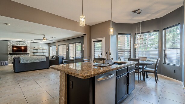 A modern kitchen with granite countertops, stainless steel appliances, and a dining area with a table and chairs. - Moore House ~ Downtown Gilbert w/ Pool & Yard Games (Gilbert)