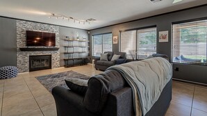A modern living room with a fireplace, a large flat-screen TV, and a sectional sofa. - Moore House ~ Downtown Gilbert w/ Pool & Yard Games (Gilbert)