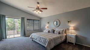 A bedroom with a bed, nightstands, a ceiling fan, a window with curtains, and a view of trees. - Moore House ~ Downtown Gilbert w/ Pool & Yard Games (Gilbert)