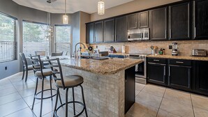 A modern kitchen with dark cabinets, a granite countertop, and a central island with bar stools. - Moore House ~ Downtown Gilbert w/ Pool & Yard Games (Gilbert)