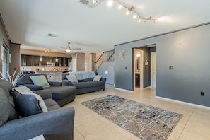 A modern living room with a gray sectional sofa, a patterned rug, and a kitchen in the background.