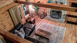 Un acogedor interior de cabaña con chimenea de piedra, sofá de cuero y una mesa de centro de madera.