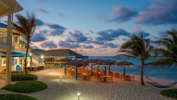 Ein Hotel direkt am Strand mit Außenbestuhlung, Palmen und Meerblick.