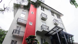 Un edificio de varios pisos con balcones, una sección vertical roja y una entrada de vidrio.