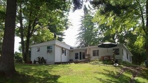 Une maison mobile à deux étages, dotée d’un porche couvert et d’un petit garage attenant, le tout entouré d’arbres.