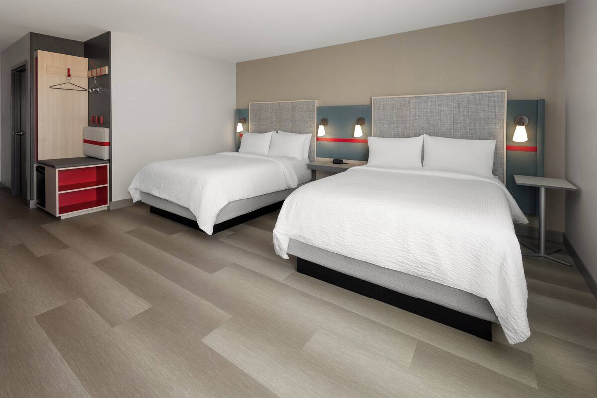 A hotel room with two beds, a wardrobe, and bedside tables with lamps.