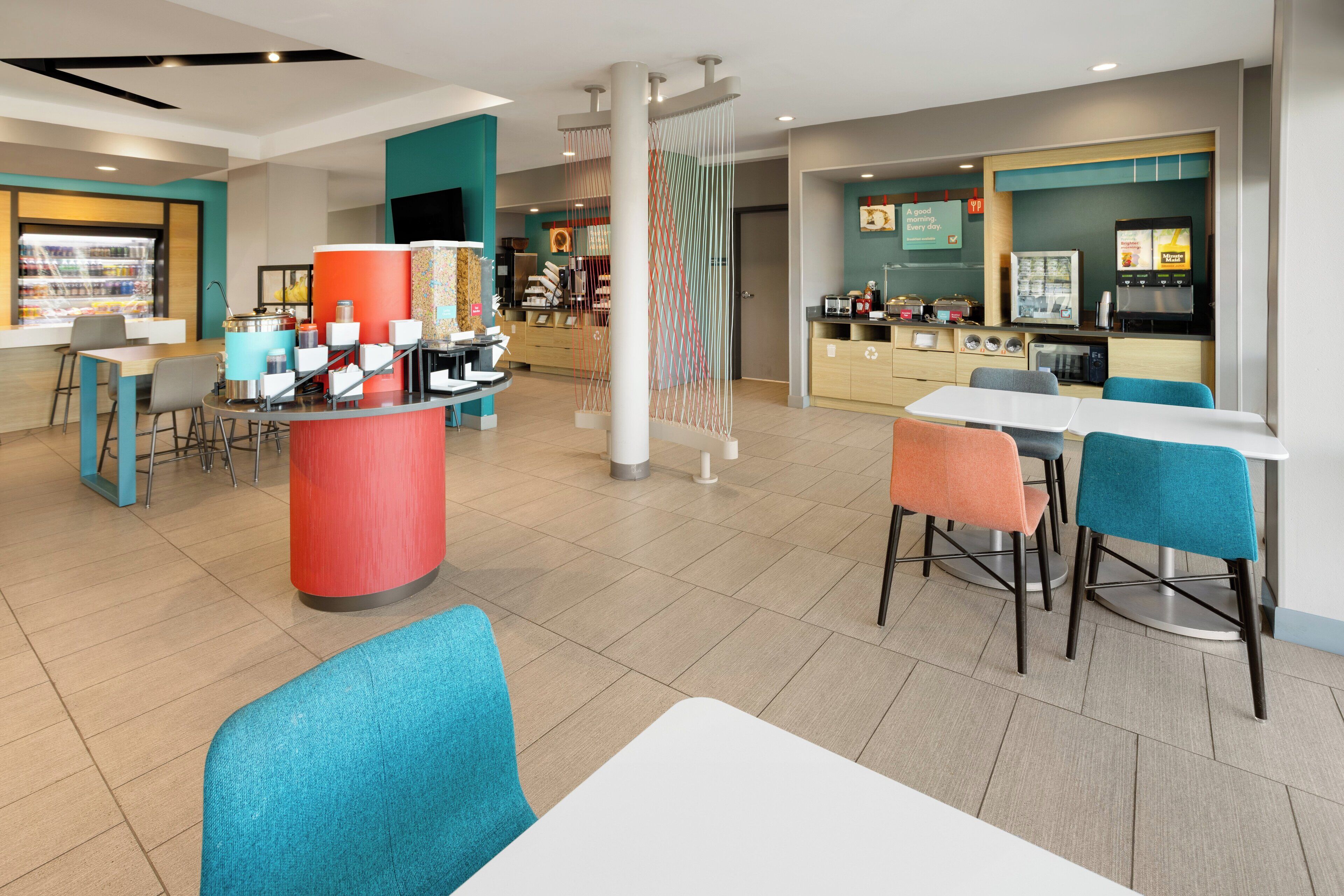 Una cafetería moderna con mostrador central, zona de mesas y exhibición de productos alimenticios.