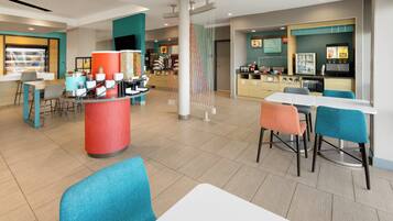 Una cafetería moderna con mostrador central, zona de mesas y exhibición de productos alimenticios.