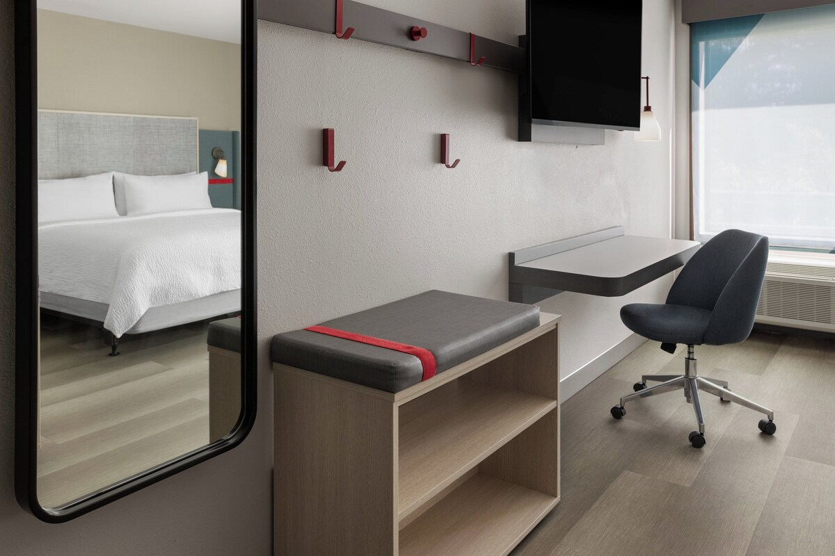 A modern hotel room with a bed, a desk, a chair, and a large mirror.