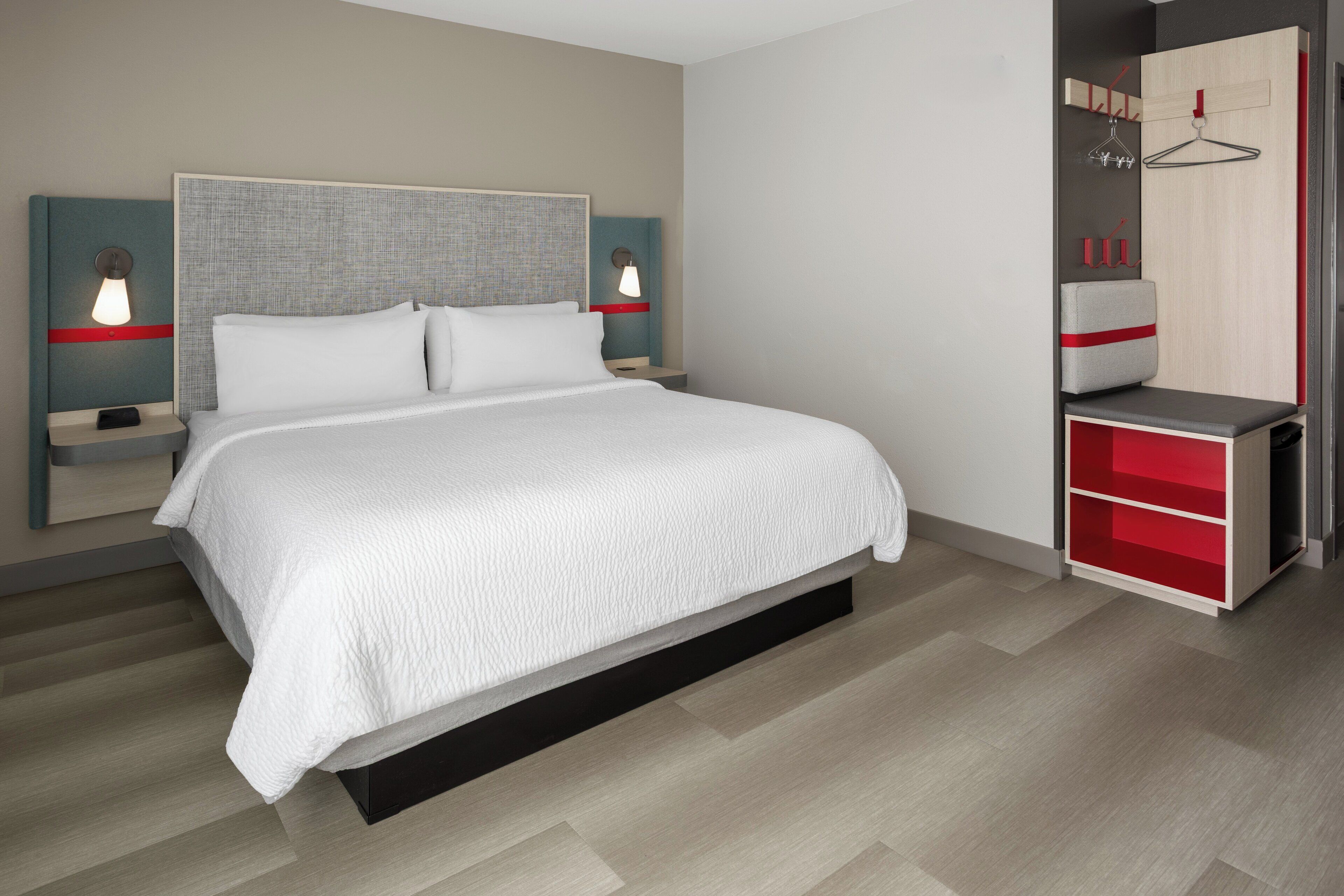 A modern hotel room with a large bed, bedside tables with lamps, a wardrobe, and a desk.